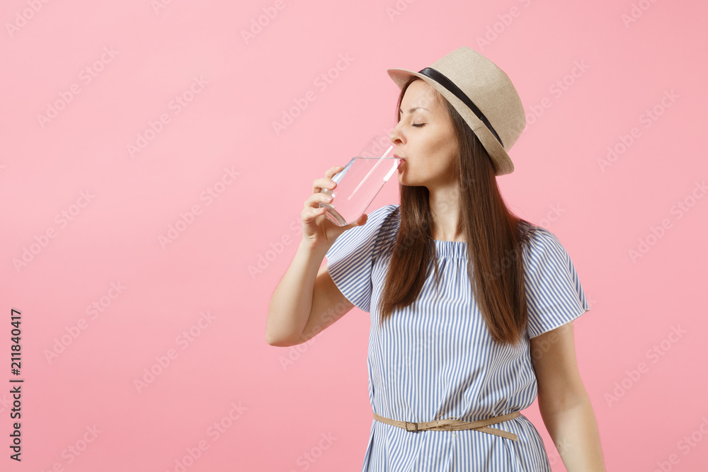 Portrait of young beautiful woman in blue dress, hat holding and drinking clear fresh pure water from glass isolated on pink background. Healthy lifestyle, people, sincere emotions concept. Copy space Portrait of young beautiful woman in blue dress, hat holding and drinking clear fresh pure water from glass isolated on pink background. Healthy lifestyle, people, sincere emotions concept. Copy space