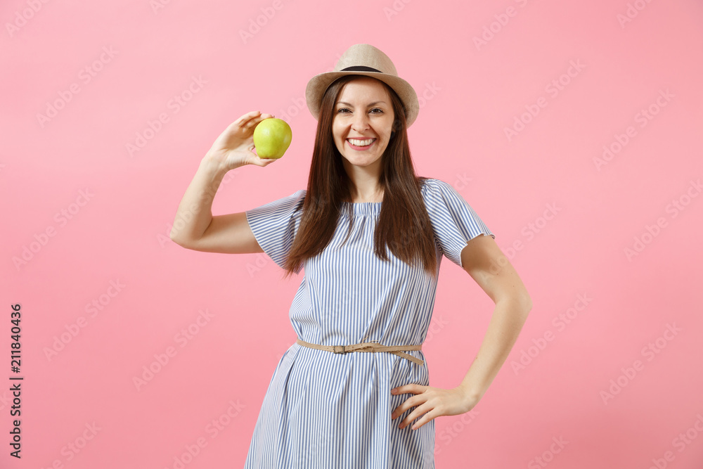 Portrait of young beautiful woman in blue dress, summer straw hat holding, eating green fresh apple fruit isolated on pink background. Healthy lifestyle, people, sincere emotions concept. Copy space. Portrait of young beautiful woman in blue dress, summer straw hat holding, eating green fresh apple fruit isolated on pink background. Healthy lifestyle, people, sincere emotions concept. Copy space.