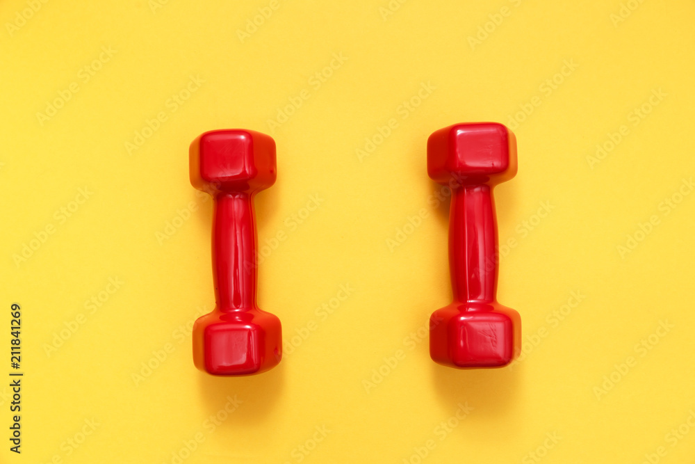 Two red womens dumbbells on yellow background Two red womens dumbbells on yellow background
