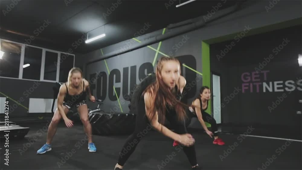 Young athletic woman jumping and exercising in team in modern dark gym. Young athletic woman jumping and exercising in team in modern dark gym.