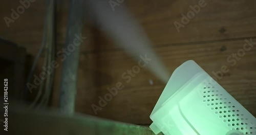 Handheld footage of an Illuminated smoke machine on stairs in front of wood wall emits smoke