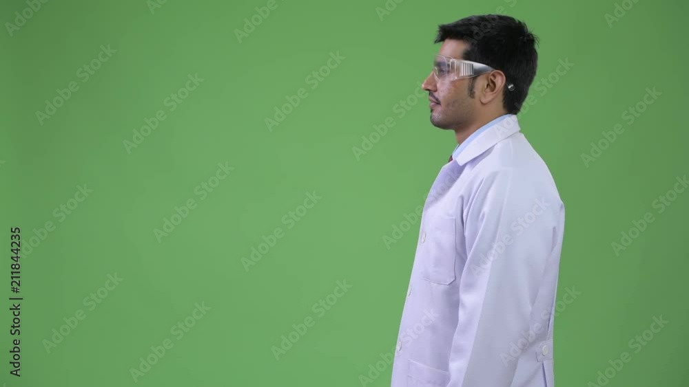 Profile view of young handsome Persian man doctor wearing protective glasses Profile view of young handsome Persian man doctor wearing protective glasses