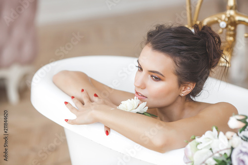 Young beautiful woman taking bath with flowers and milk