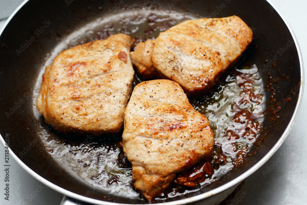A close up of greasy pieces of pork in a frying pan. A close up of greasy pieces of pork in a frying pan.
