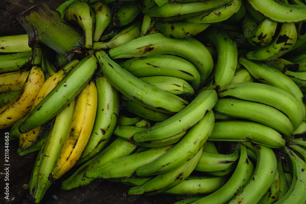 A store selling only bananas. Raw and ripe green and yellow bananas in bunches, lying on the table and the floor.