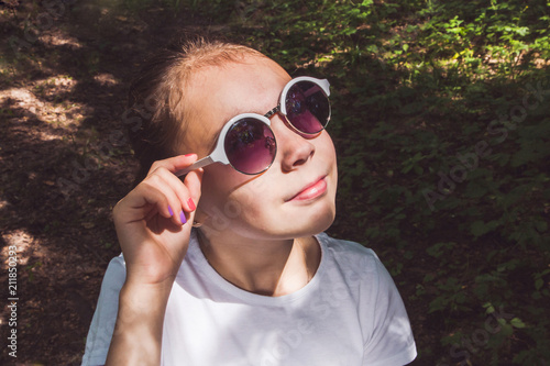 Happy little girl with sunglasses looking at the sun in the summer forest