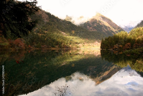 On a calm morning in Sichuan  China  Jiuzhaigou   s    Mirror Lake    reflects the Min mountains  along with the fall foliage and cloud cover  creating a peaceful  yet stunning scene.