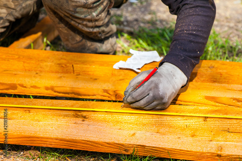 The builder left-handed measures the tape measure with a pencil and marks with a pencil © Sergey