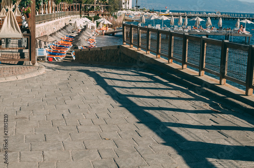 A pedestrian road along the beautiful promenade for walks and sports in Bodrum, in the background the sea, sandy beach, sun loungers and beach umbrellas, pier. photo