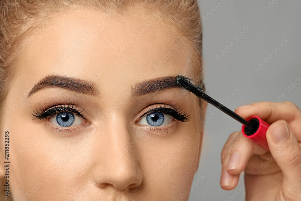 Young woman undergoing eyebrow correction procedure on grey background, closeup