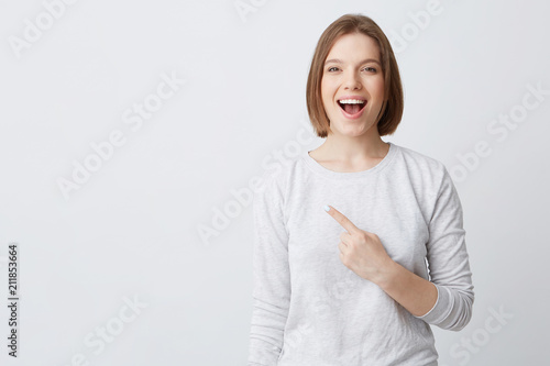Wallpaper Mural Happy excited young woman in longsleeve with opened mouth feels confident and pointing to the side isolated over white background Torontodigital.ca