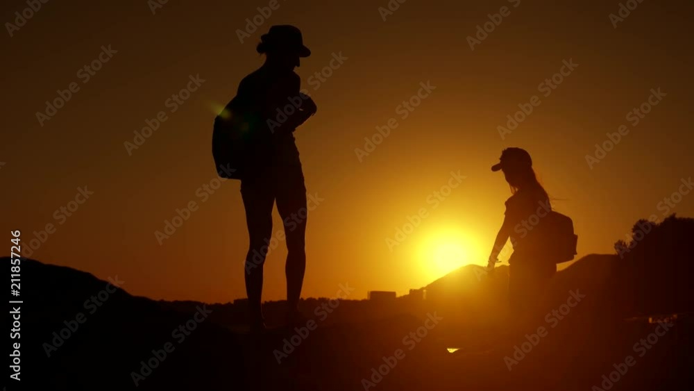 Silhouettes of mother and child tourists hiking at sunset. Mom and daughter on summer vacation carrying backpacks. Little girl following her mom on cliff edge. The concept of traveling with children. Silhouettes of mother and child tourists hiking at sunset. Mom and daughter on summer vacation carrying backpacks. Little girl following her mom on cliff edge. The concept of traveling with children.