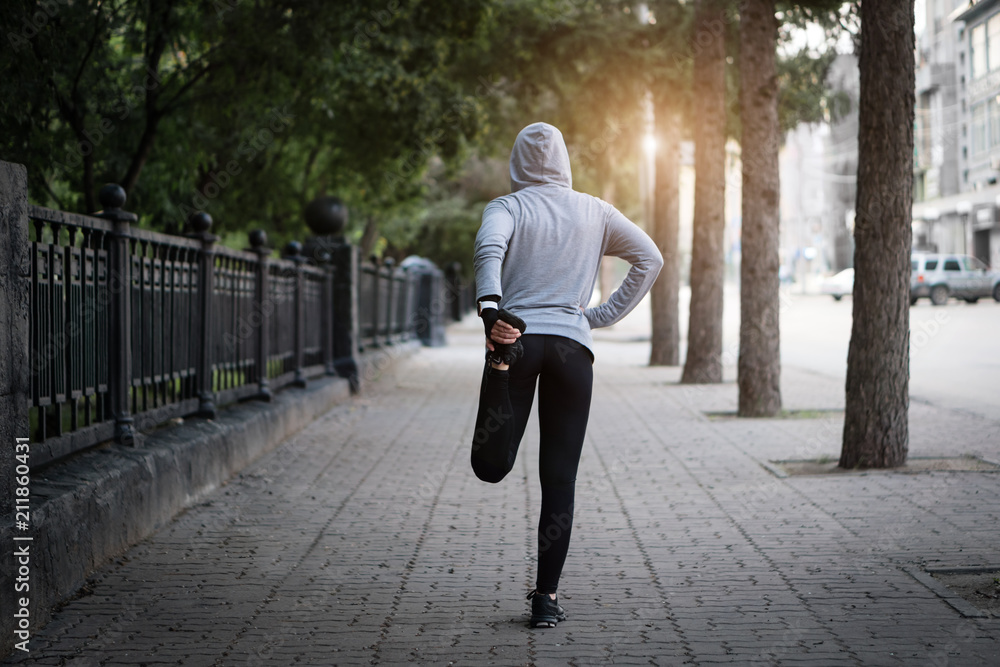 Running stretching. Woman athlete on a city street doing exercises.