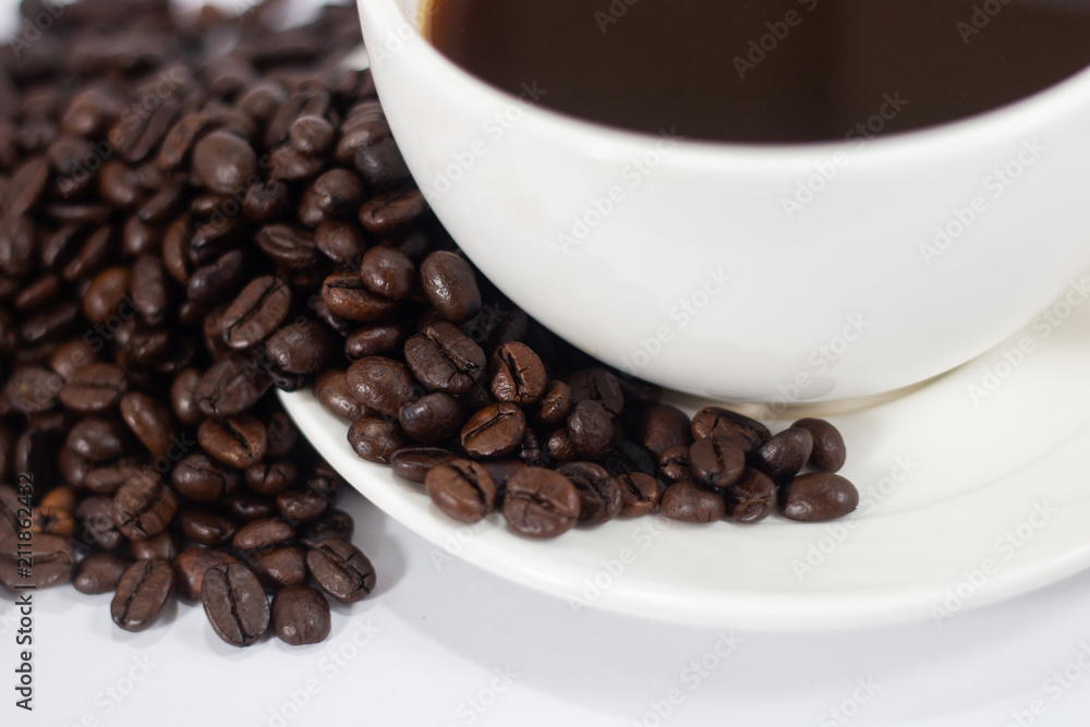 Fototapeta premium coffee beans heap with white cup and saucer . black and brown color seeds background . close up nutrition textured