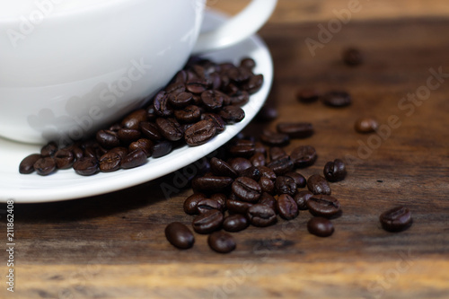 coffee beans with white cup and saucer . black and brown color seeds on wooden table background .