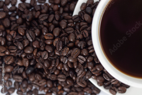 coffee beans heap with white cup and saucer . black and brown color seeds background . close up nutrition textured