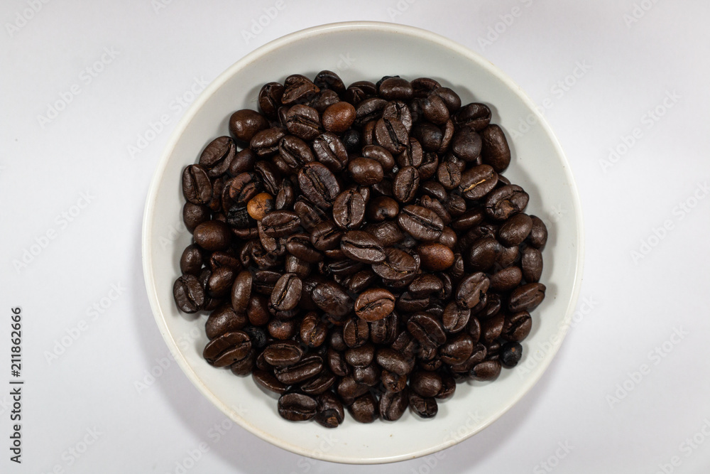 close up texture coffee beans heap with white saucer . black and brown color seeds isolated white background . close up texture coffee beans heap with white saucer . black and brown color seeds isolated white background .