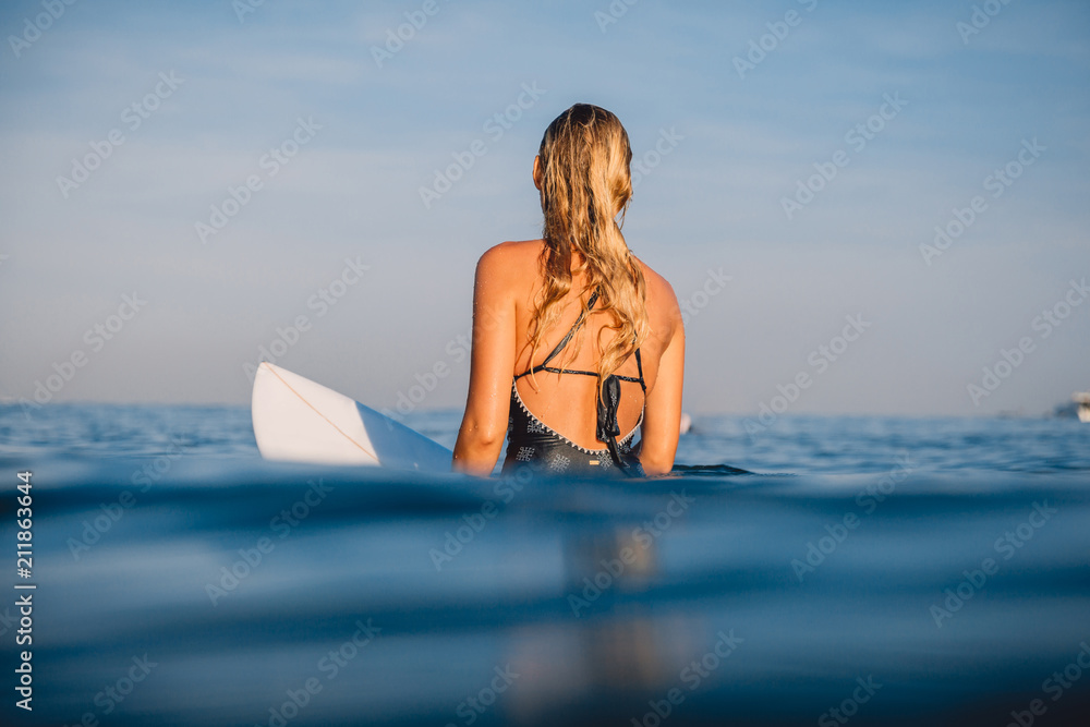Surfer woman sit at surfboard. Woman with surfboard in ocean