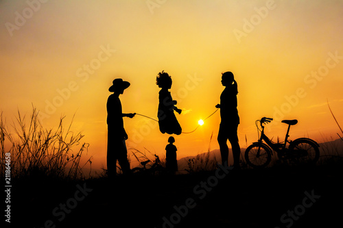 Silhouette group of happy children playing on mountain at sunset, summer time