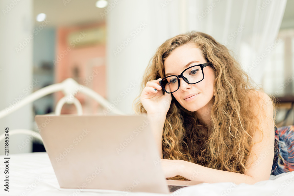 Happy young woman is sitting relax playing laptop on bed at her bedroom.woman working on laptop while sitting at his working place in her home Happy young woman is sitting relax playing laptop on bed at her bedroom.woman working on laptop while sitting at his working place in her home