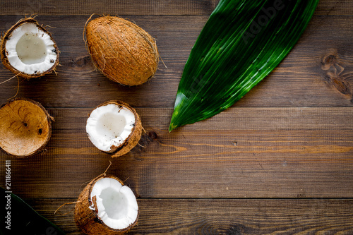 Tropical composition with coconut. Whole coconuts and coconut cut in half near pulm leaves on dark wooden background top view copy space