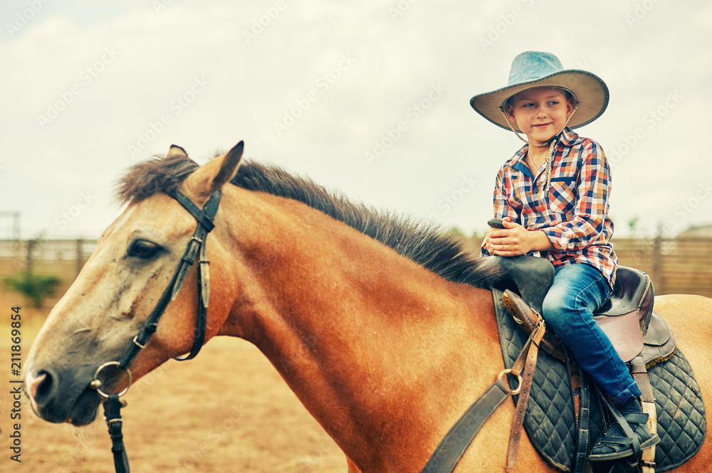 The boy is sitting on a horse . A child on a day walk on the ranch
