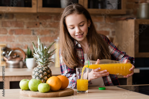 child health and development. useful and tasty drink. vitamin orange juice for balanced nutrition. little girl pouring fresh fruit beverage from a bottle