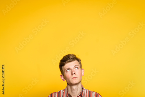 uncomprehending bewildered puzzled perplexed wondering man looking upwards. portrait of a young guy on yellow background pop up or peek out from the bottom. free space for advertising. photo