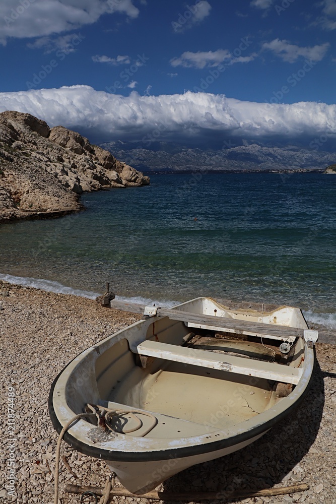 White faded fiberglass fishing boat on rocky beach surrounded by large rocks. Location near Vrsi village, Croatia, Adriatic