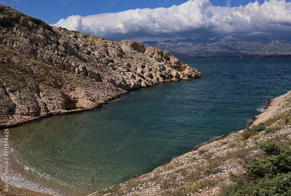Two rocky cliffs creating narrow bay with small stones on shore, emerging dense clouds in mountanis in background. Location  Croatia, Adriatic sea