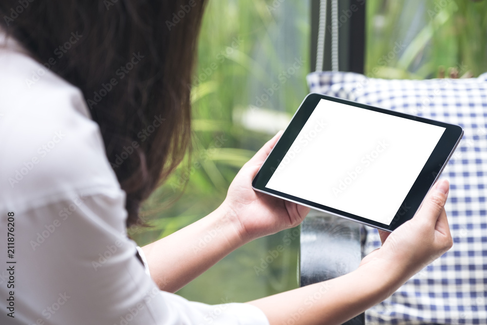 Mockup image of woman holding black tablet pc with blank white desktop screen and green nature background