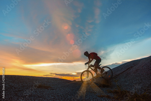 silhouette of a man riding a mountain bike down from a hill, extreme sport mountain biker with sunset scenery in background