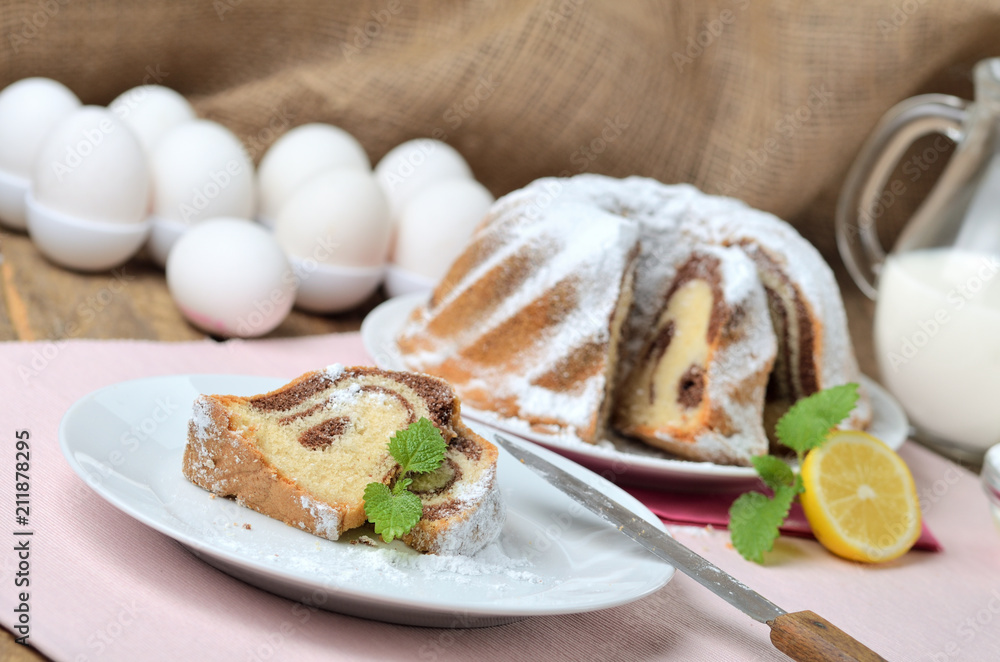 Cut of marble cake sprinkled with sugar, lemon, melissa, milk, eggs and butter