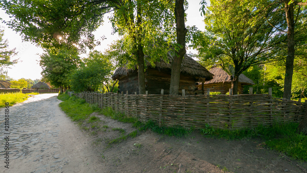 a wooden house with a reed roof near a wicker tin under high trees a wooden house with a reed roof near a wicker tin under high trees