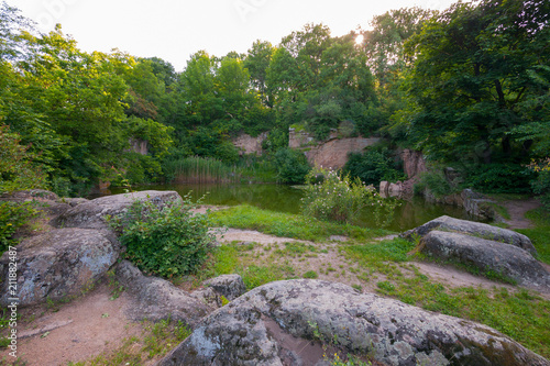 A small green transparent lake on a background near stone boulders and green vegetation