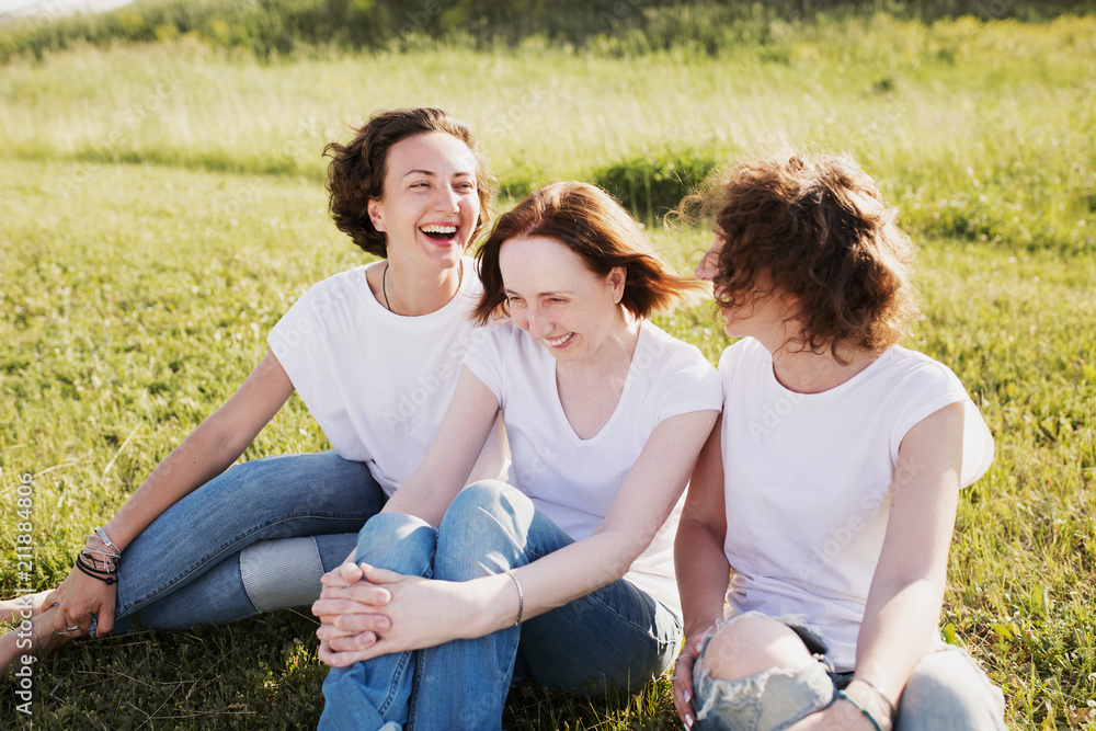 Picnic in nature. Pretty woman mother of two adults beautiful funny daughters rest on the meadow talking about something on a sunny summer day Picnic in nature. Pretty woman mother of two adults beautiful funny daughters rest on the meadow talking about something on a sunny summer day
