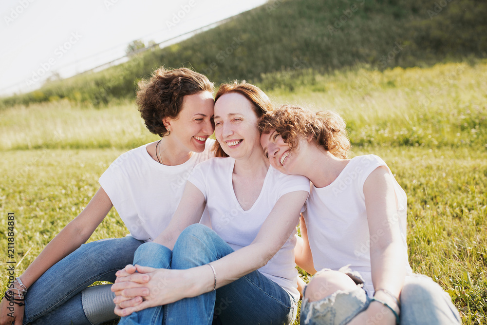 Picnic in nature. Pretty woman mother of two adults beautiful funny daughters rest on the meadow talking about something on a sunny summer day