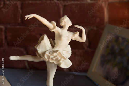 White porcelain statuette of a ballerina against a brick wall background photo