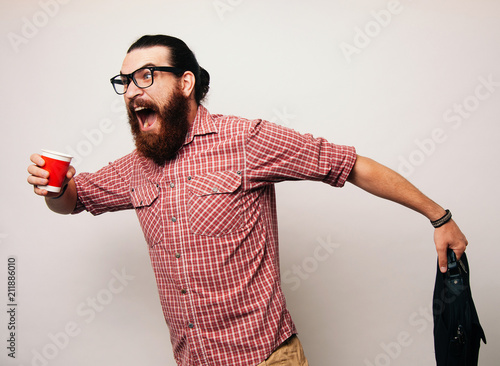 Young bearded man running wearing glasses, is late to work, coffee to go. Young man scared to be late, in a hurry or rush. Rush hour concept. photo