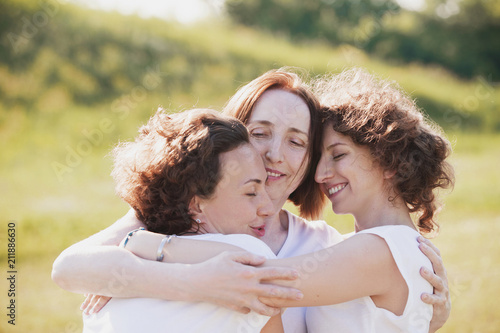 Three pretty women mum and two adult daughters embrace while walking outside the city on a background of a blurred picturesque hill