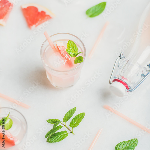Flat-lay of cold refreshing summer alcohol cocktail with fresh grapefruit, mint and ice over white marble background, selective focus, square crop
