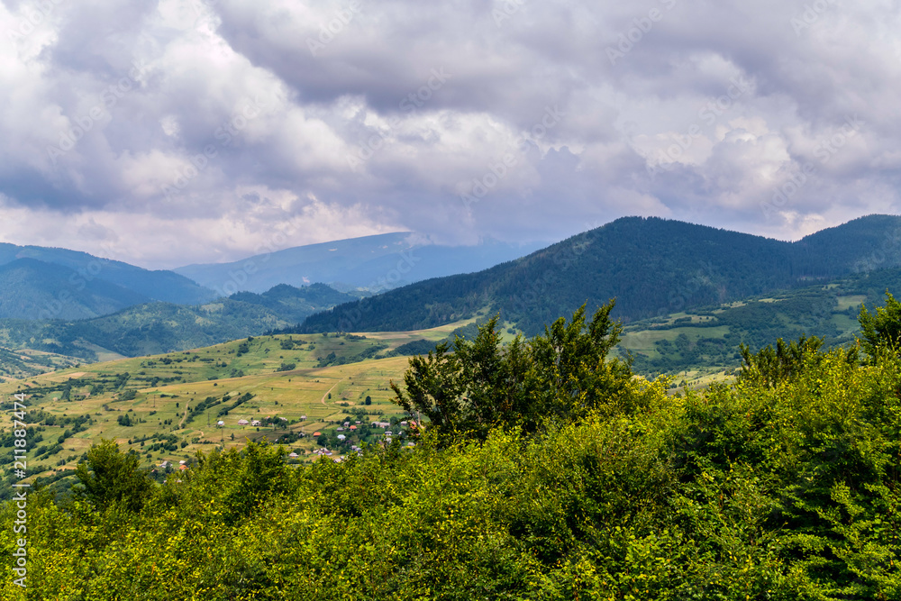A gray cloudy sky stretching over a small rural village in the shadow of the huge green Carpathian mountains