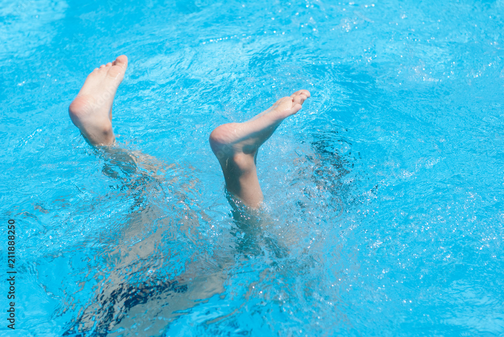 two legs of diving child on water surface of azure summer outdoor swimming pool
