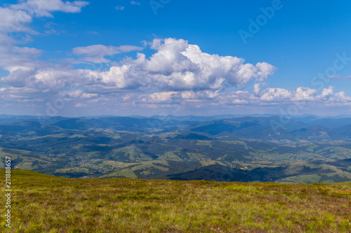 A beautiful view from the top on the huge green mountains and a small rural village at their foothills © adamchuk_leo