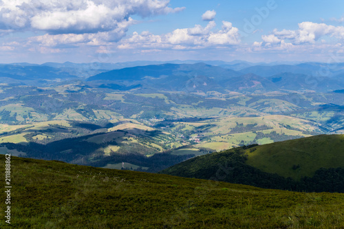 Green fields, deciduous forests and a small rural village at the foot of the summit of a huge mountain