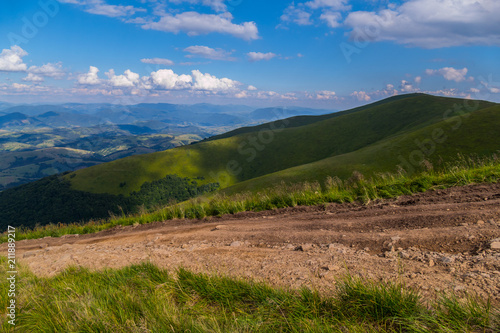 A steep dodgy dusty road leading to the descent from a wide green mountain