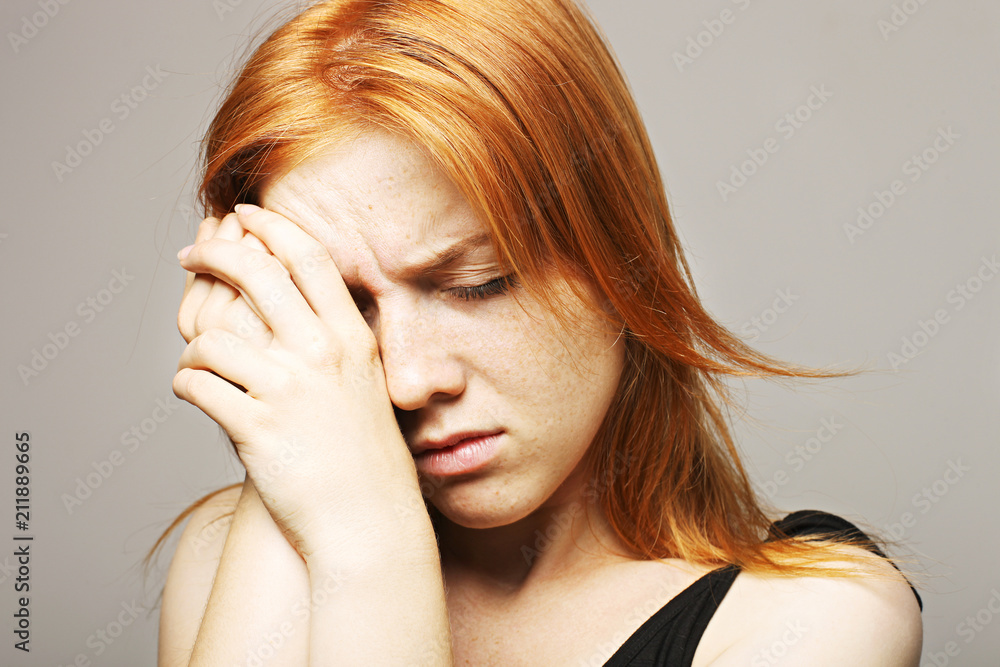 Naklejka premium Beautiful fragile redheaded young woman in the dark. Sad frightened girl scared of abuse. Nonverbal behavior, body language. Red hair female looking stressed out & depressed. Background, close up.