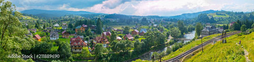 Panoramic photo of a small city with colorful houses, a river and a railway. And all this against the background of greenery
