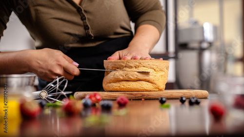 The pastry chef prepares a biscuit cake in the home kitchen or in a restaurant. The concept of the process of making cakes for restaurants, cafes and bars. on the photo the girl hands cuts a biscuit