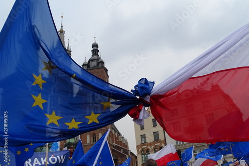 Związana flaga Unii Europejskiej i Polski, demonstracja w Krakowie, widoczna część napisu Kraków, w tle architektura rynku, wieże kościoła mariackiego